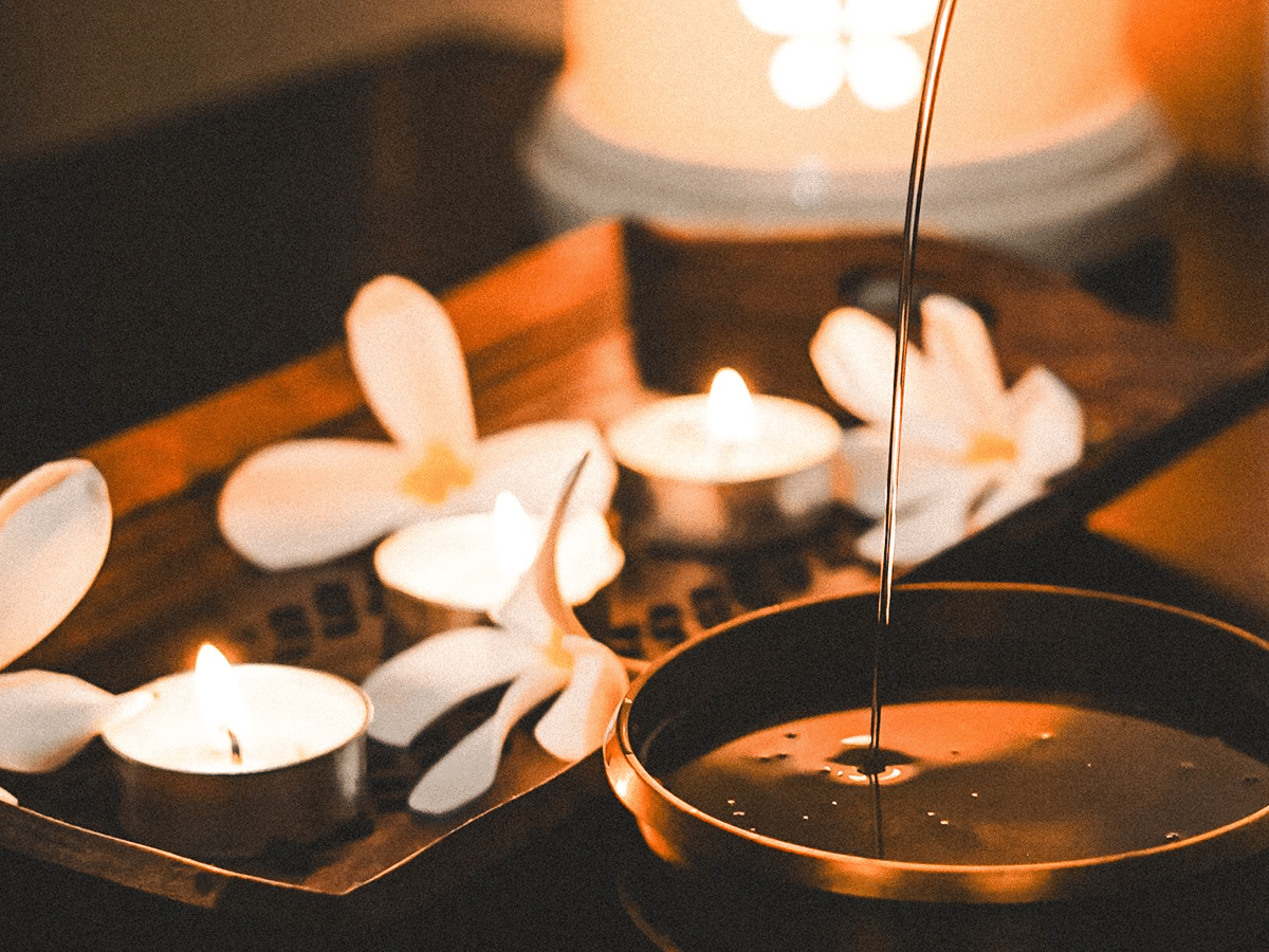 Warm massage oil poured into a bowl beside lit candles and white flowers in the Ayurvedic spa at The Garud Forest, Tadoba