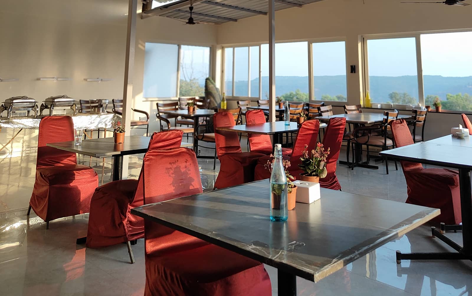 The Sahyagirija restaurant hall with red chairs and tall windows onto the valley