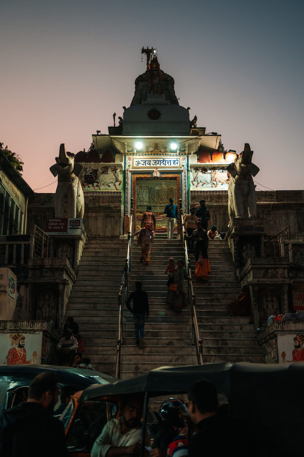 Jagdish Temple Udaipur entrance lit up at dusk with devotees climbing the marble steps between two stone elephant statues