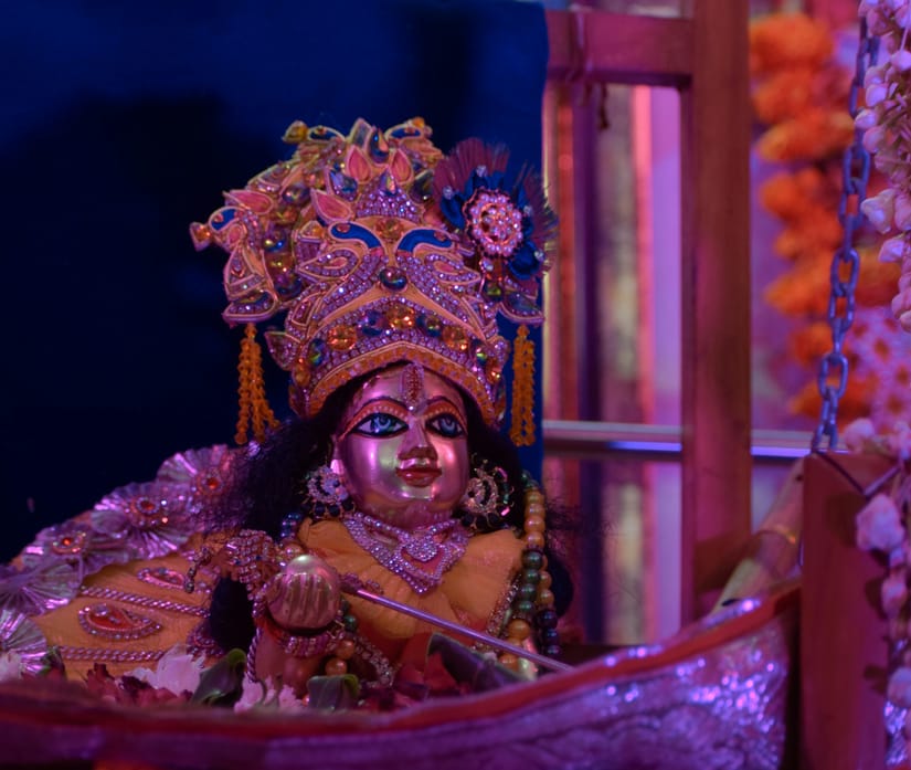Elaborately decorated idol of baby Krishna surrounded by flowers and lamps during temple darshan in Udaipur