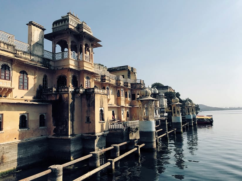 Historic stone buildings with ornate pavilions along a serene lake waterfront