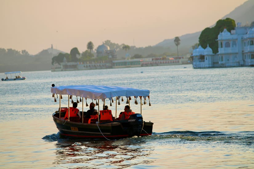 Wooden boat crossing the calm waters of Lake Pichola in Udaipur with the City Palace and hills in the background