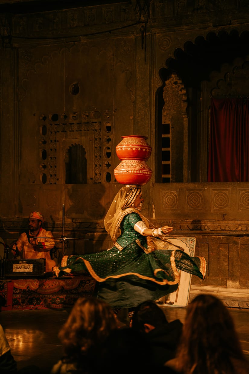 A dancer in a traditional green dress balancing multiple stacked clay pots on her head
