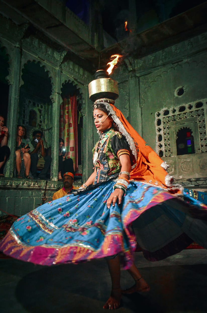 A dancer in a colorful ghagra spinning with a flaming pot balanced on her head at Bagore Ki Haveli dance show