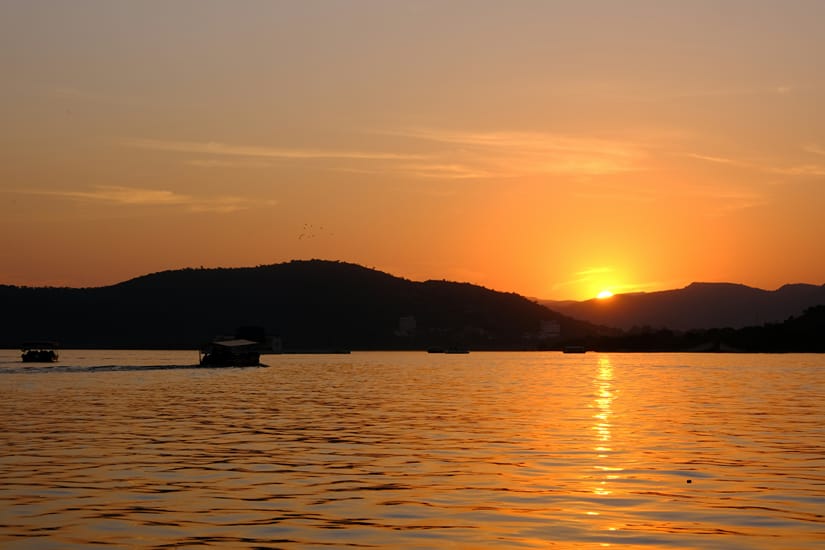 Golden sunset over Lake Pichola with silhouetted palaces and hills reflected across the water