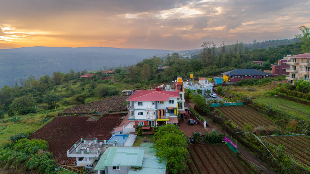 Aerial view of the resort among farm fields and trees, with the valley under a sunset sky behind
