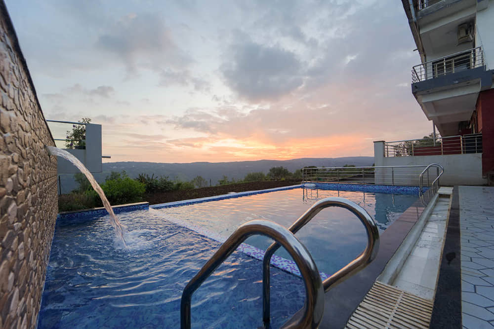 Infinity swimming pool with a waterfall spout and steel handrails beside the resort at sunset