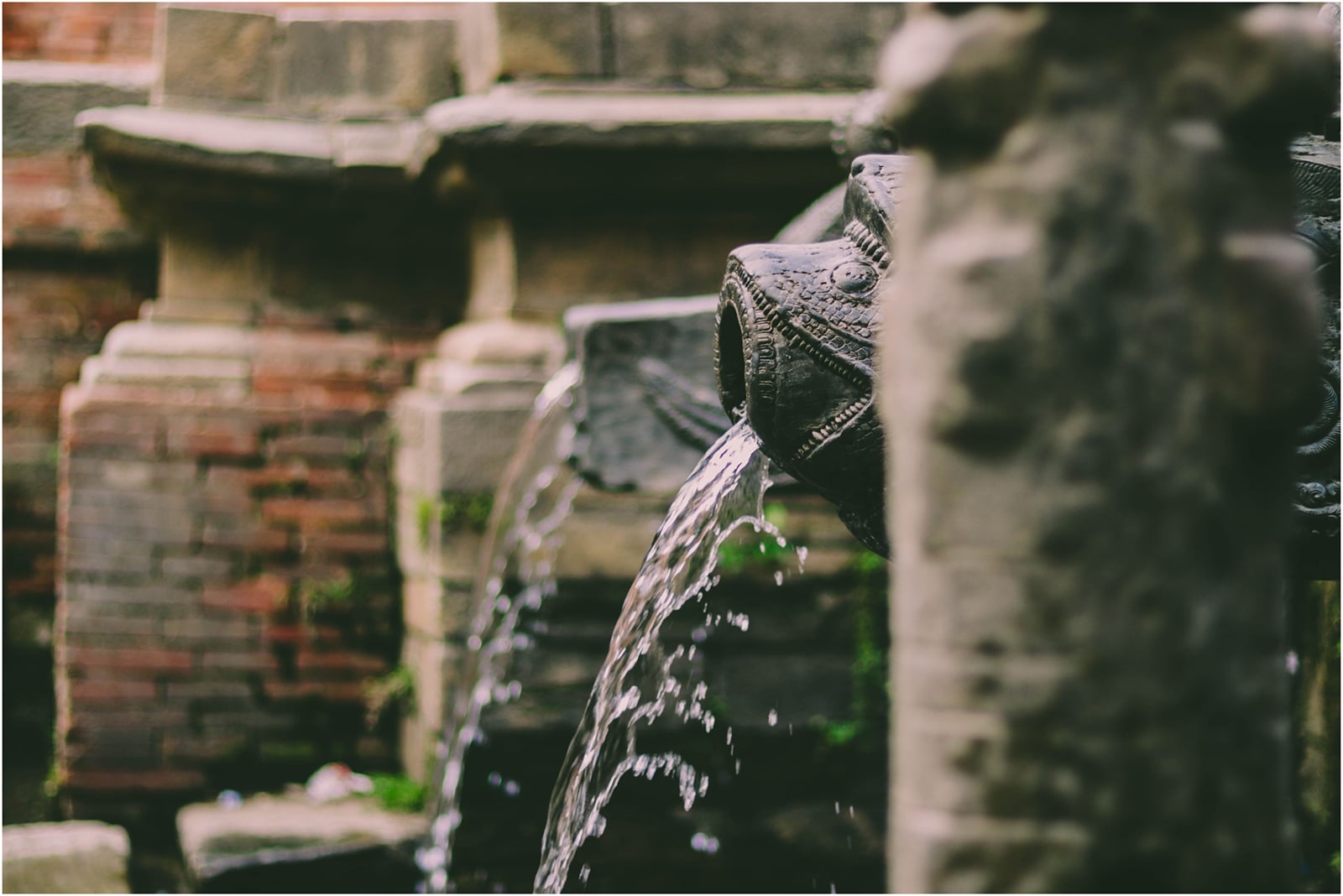 Ga Hiti, a traditional Newari stone water spout near Thamel Chowk in Kathmandu, with water running from a carved stone spout into a sunken stone basin.