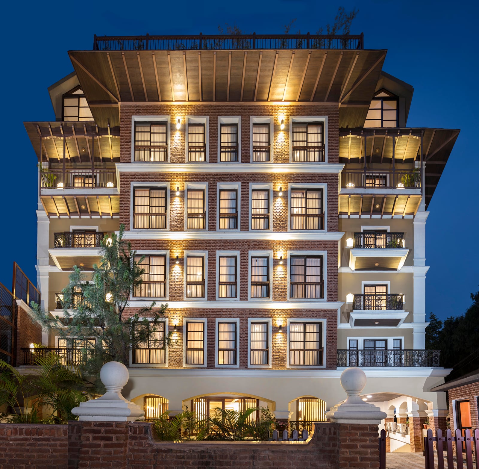 The red-brick facade of Nepali Ghar Hotel, a heritage hotel in Thamel, Kathmandu, at dusk, its balconies and arched windows warmly lit against a deep blue sky.