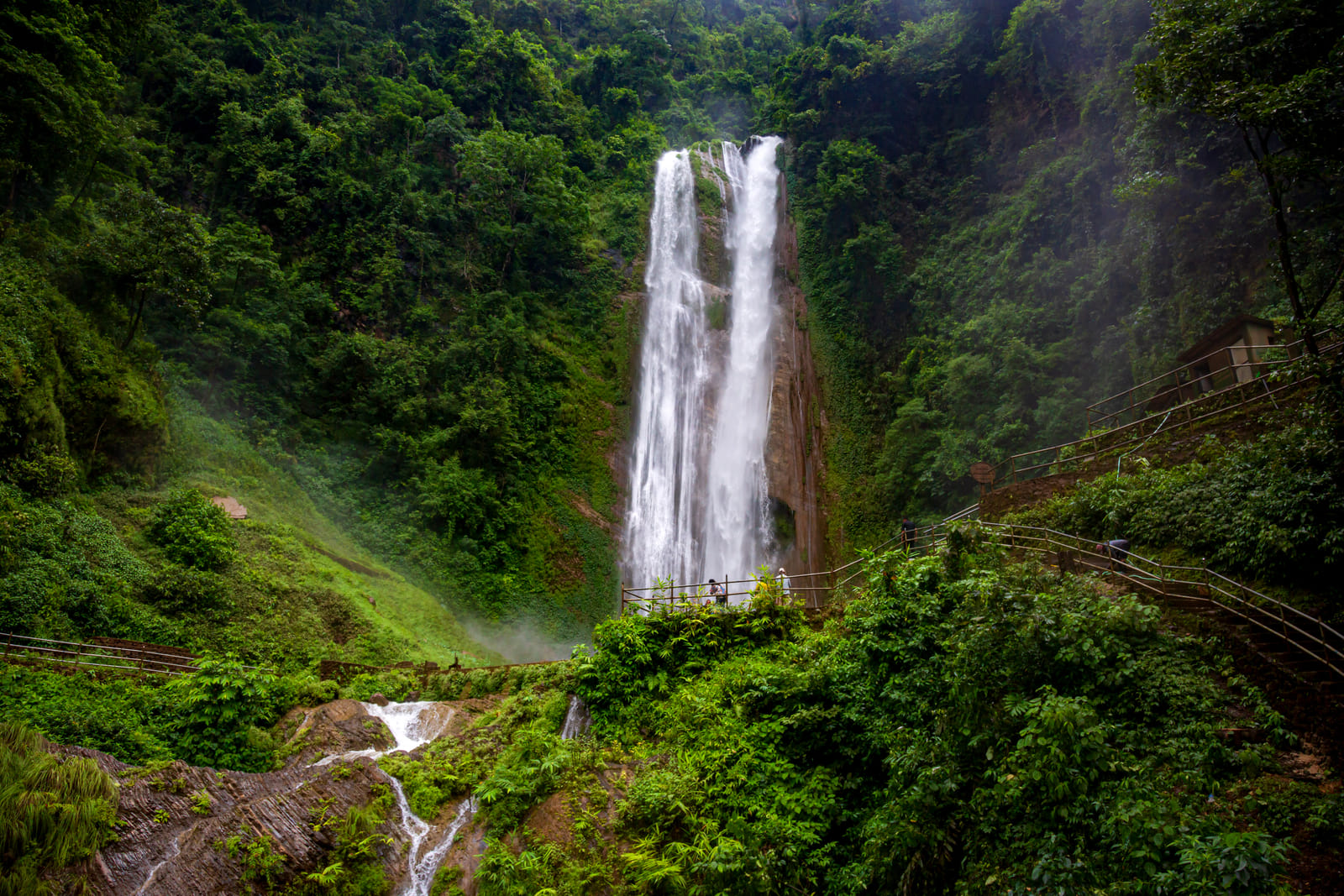A twin-stream waterfall cascading through lush green forest in Kathmandu valley during monsoon