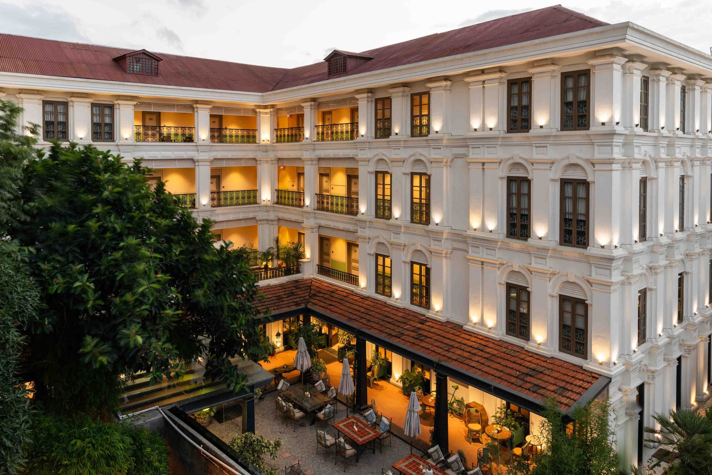 An aerial view of the Neo-Classical Wing courtyard at Nepali Ghar Hotel during the golden blue hour, its tiered colonial balconies lit warmly above the garden seating.