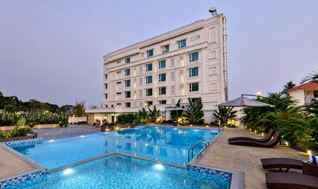 The swimming pool with sun loungers and a parasol, the hotel lit up behind it at dusk