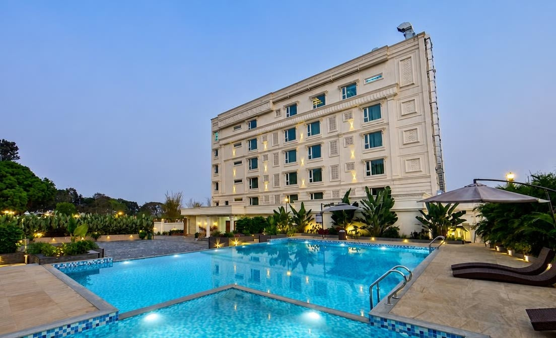 The swimming pool and planted terrace beneath the white hotel building at dusk