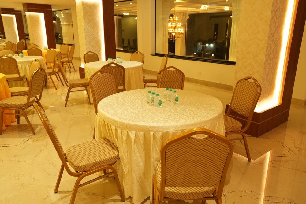 Round banquet tables and gold-framed chairs set beside the hall's picture window and backlit columns