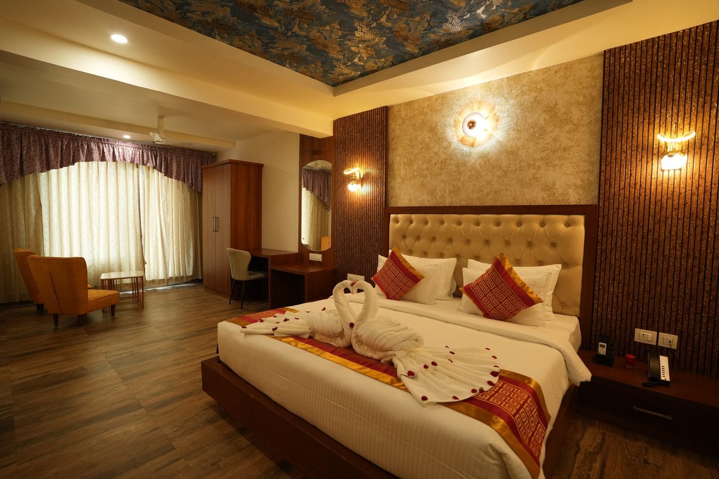 Crown Suite bedroom with a wardrobe, work desk and an armchair beside the curtained window