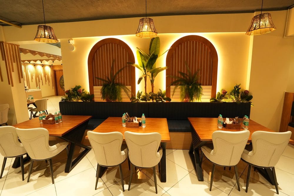 Restaurant tables and upholstered chairs laid beneath woven pendant lights and planted arched alcoves