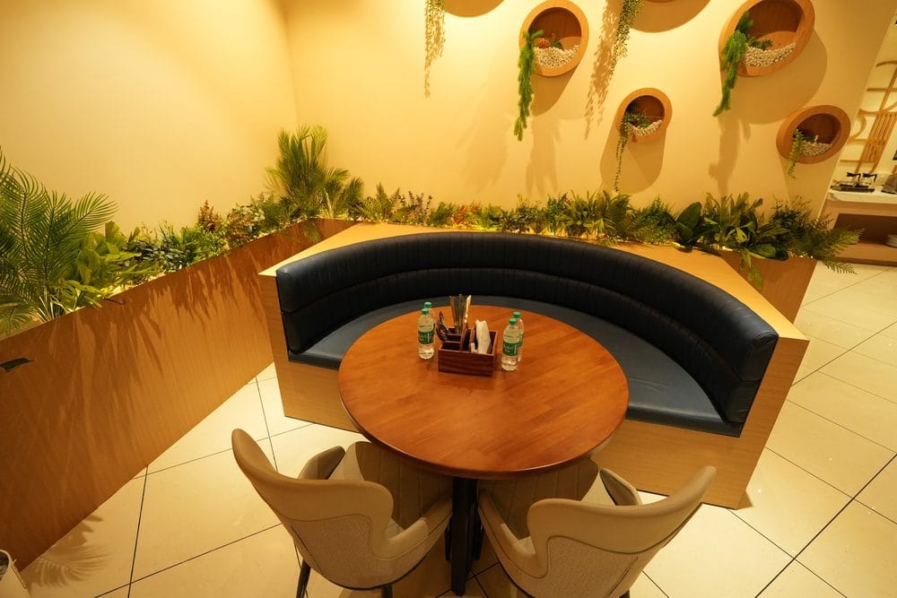 A curved private booth with a round table, surrounded by planting and a wall of potted alcoves