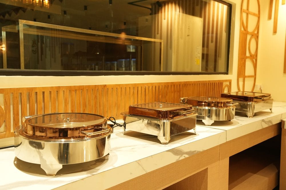 Polished chafing dishes set out along the marble buffet counter at Golden Garnish