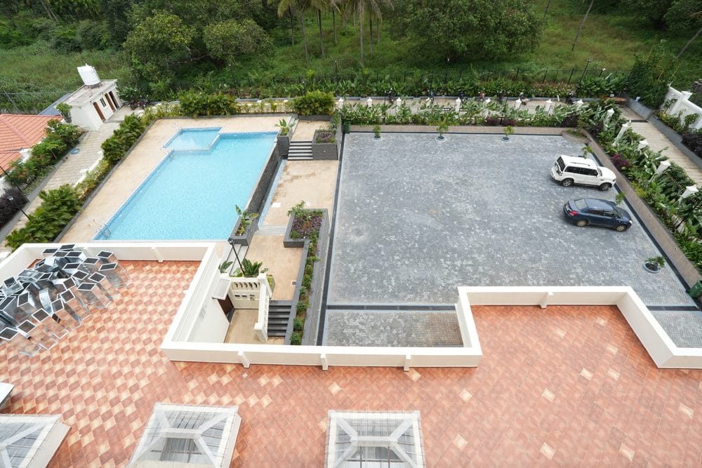 Looking down from an upper floor onto the swimming pool, terrace and parking area, with coconut palms beyond