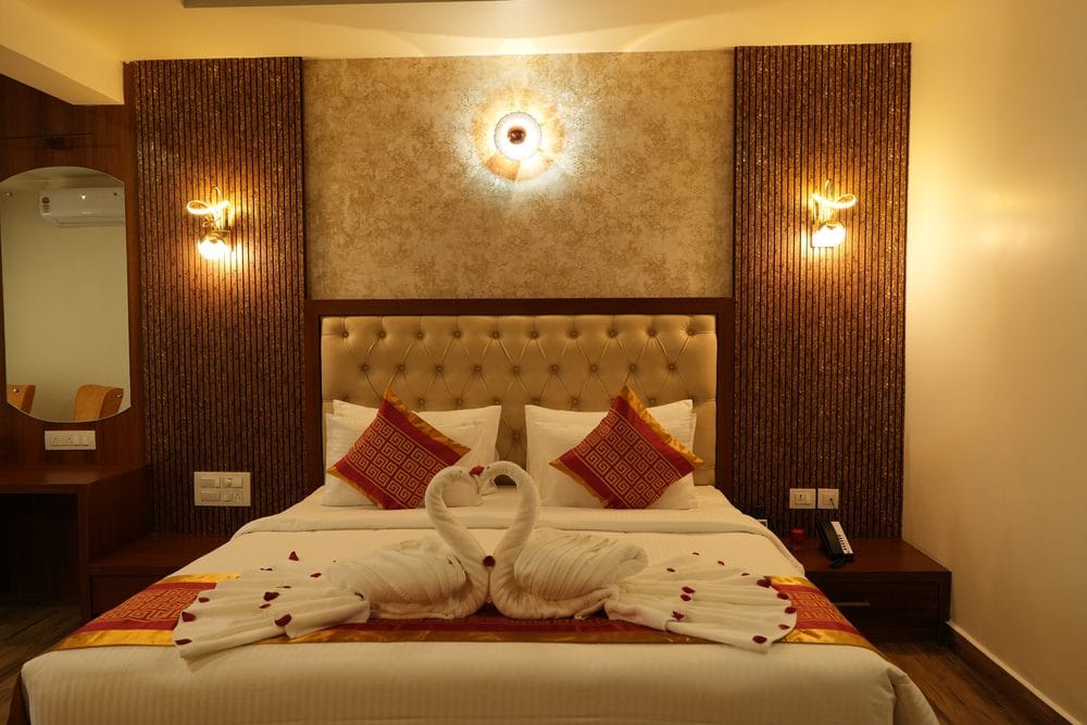 King-size bed dressed with swan towel art beneath a lit feature panel and tufted headboard