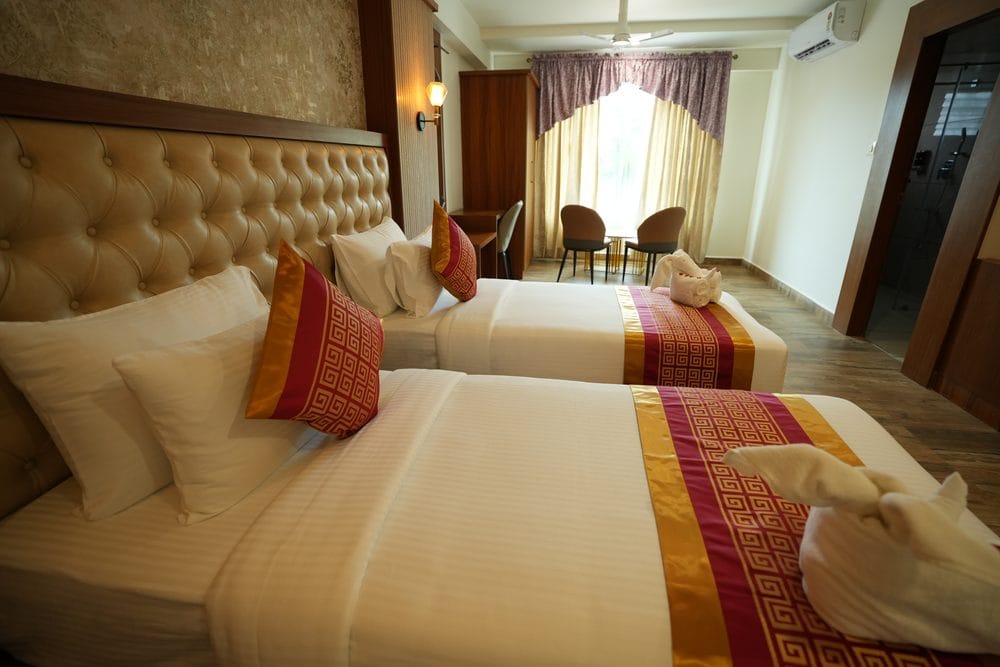 Guest room made up with twin beds, a tufted headboard and a table and chairs by the window