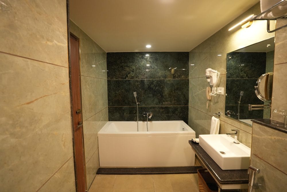 En-suite bathroom clad in green and cream marble, with a soaking tub, vanity basin and hairdryer