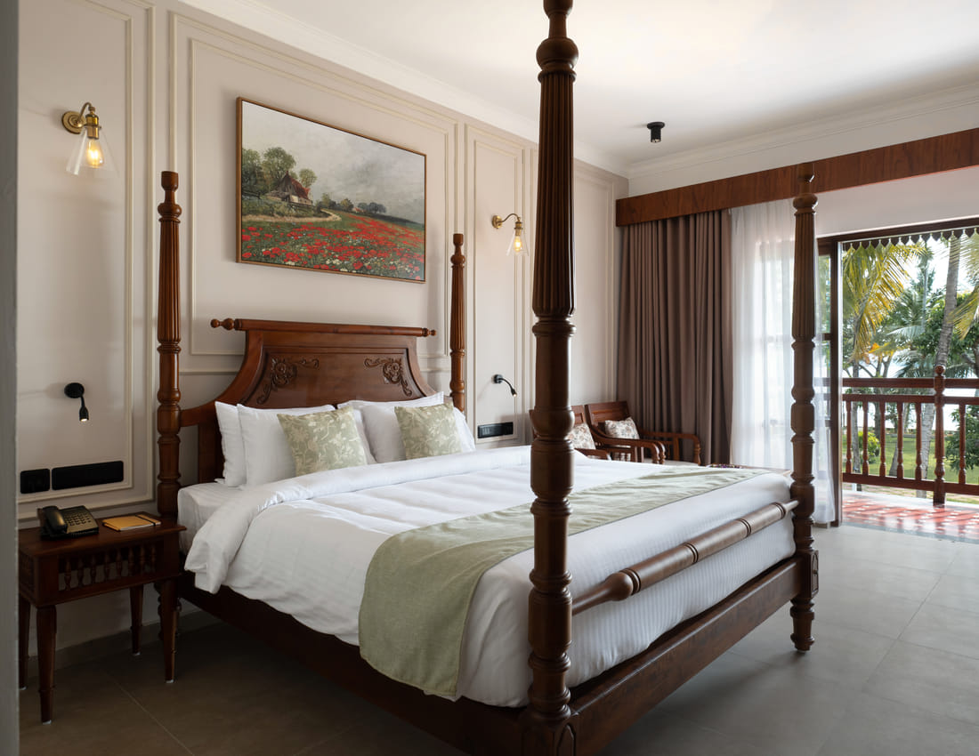 Lake View Room with a four-poster king bed and balcony doors framing palms and Vembanad Lake, Sanskreti