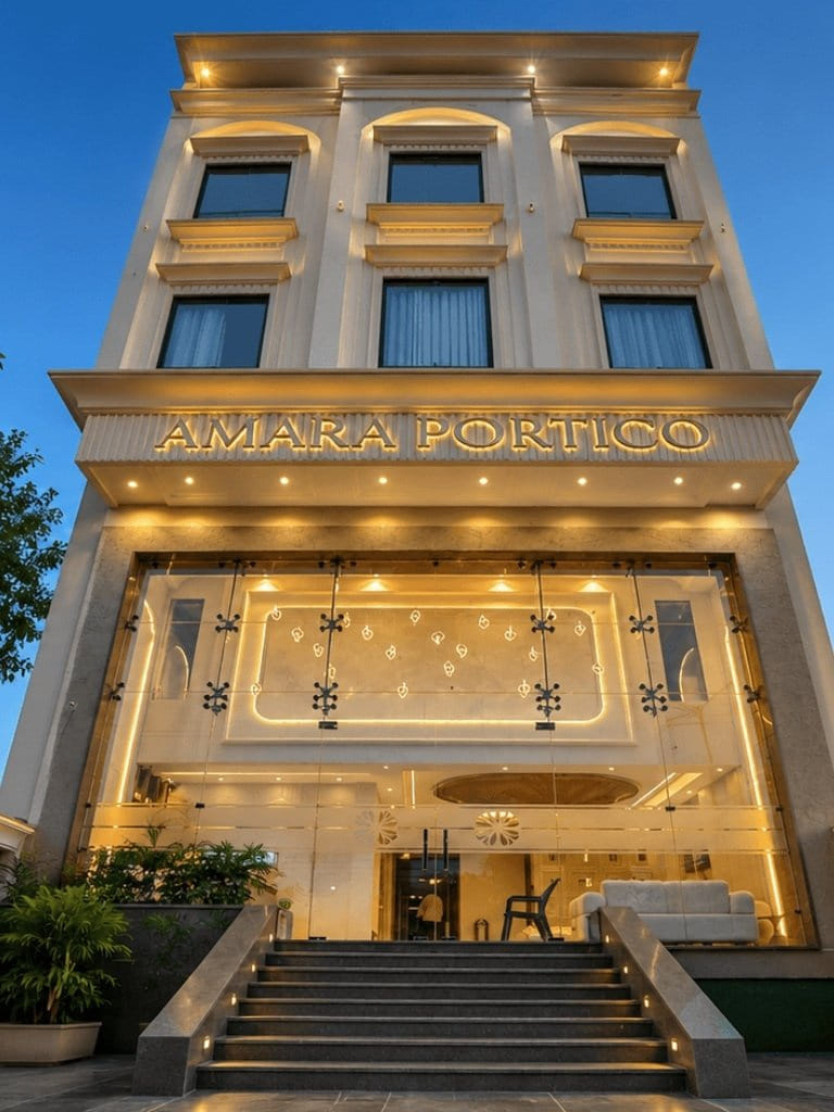 The lit facade of Amara Portico in Amritsar after dark, its gold signage above the entrance and steps rising between planters