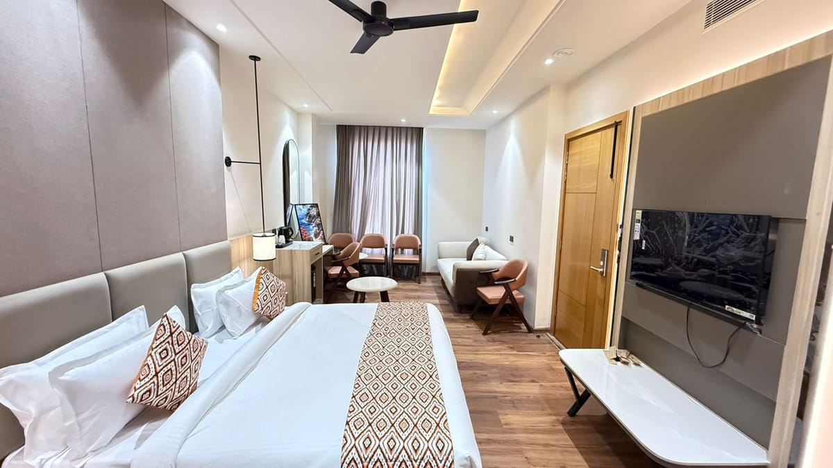 A guest room at Amara Portico, with a wide bed, a seating area of chairs and a small table, and a television on the side wall