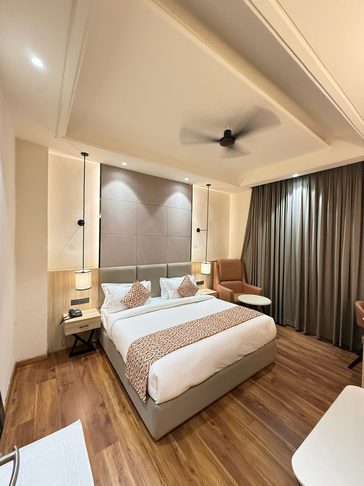 A guest room at Amara Portico, with a padded headboard, dark full-length curtains