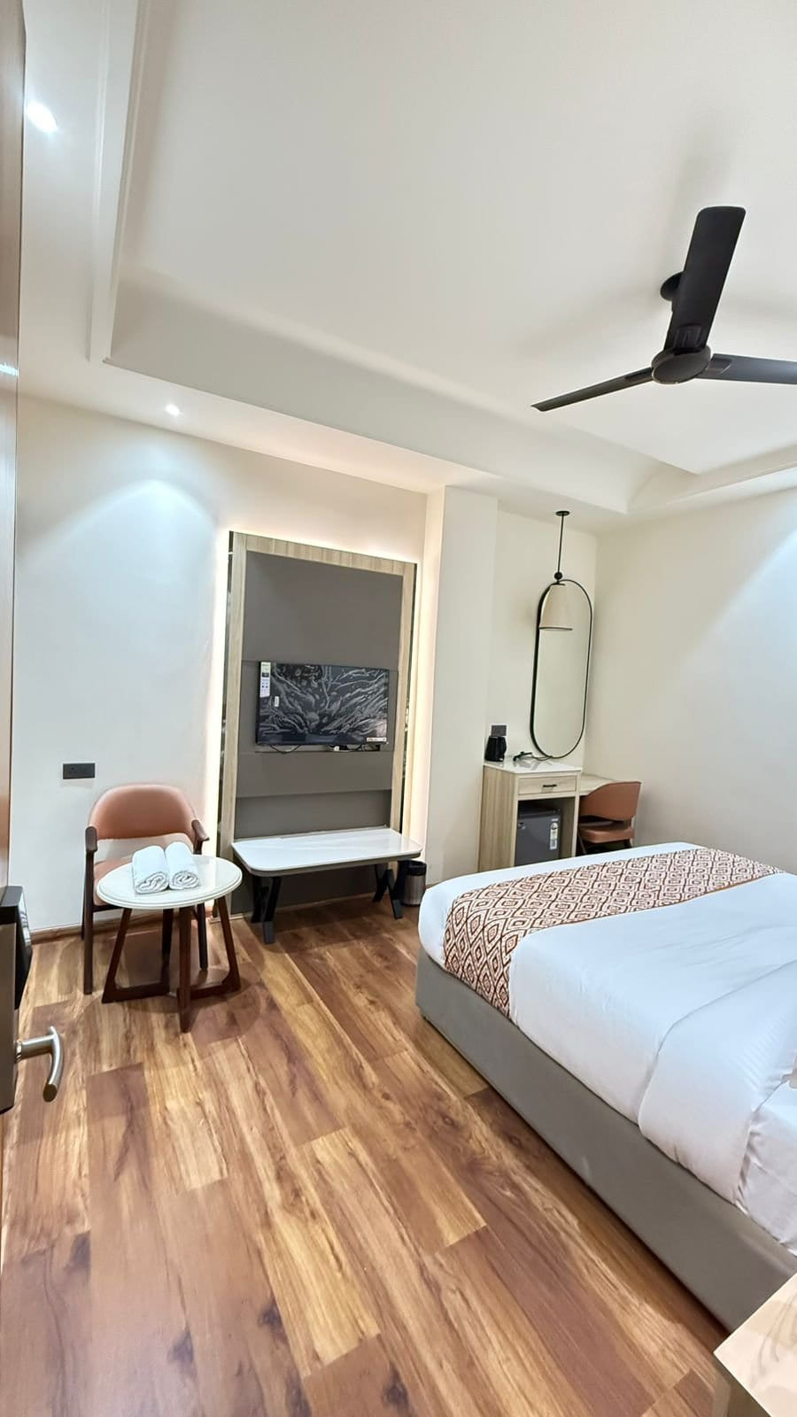 A guest room at Amara Portico, with a television opposite the bed and two chairs drawn up to a small table beside the window