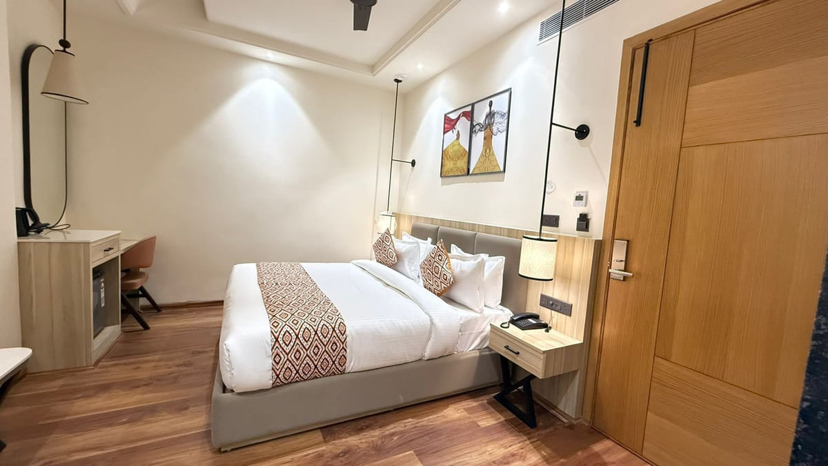 A guest room at Amara Portico, with a bed against a padded headboard, framed artwork above and a desk