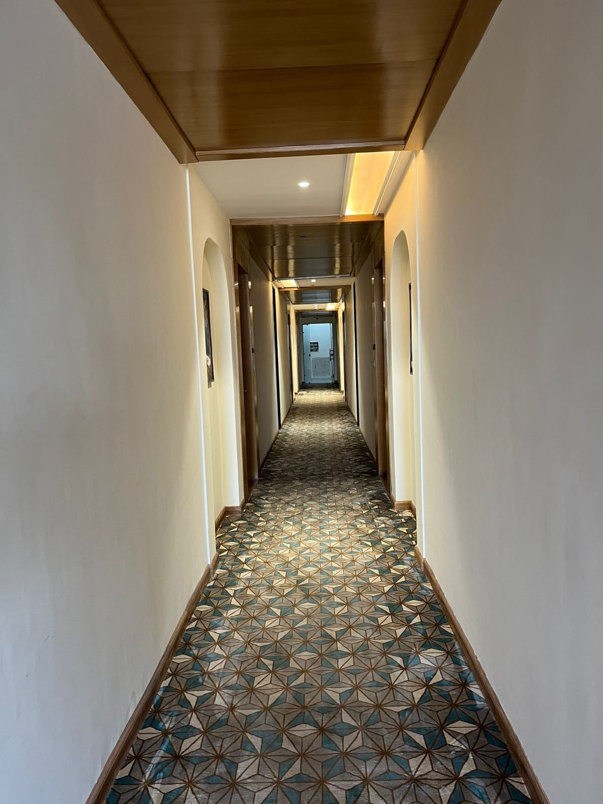 A guest room corridor at Amara Portico, running between the bedroom doors on patterned carpet under warm ceiling lighting