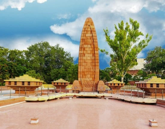 The Jallianwala Bagh memorial in Amritsar, its tall red sandstone flame rising among the garden pavilions under a bright sky