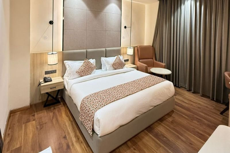The Super Deluxe Room at Amara Portico, with a patterned runner across the bed, an armchair and full-length curtains behind