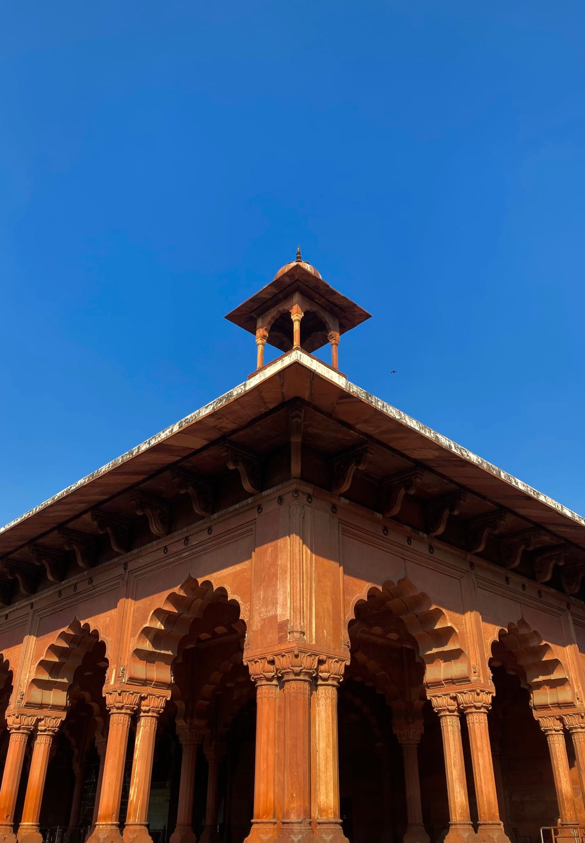 A carved red sandstone pavilion at Gobindgarh Fort in Amritsar, its columns and wide eaves set against a clear blue sky above