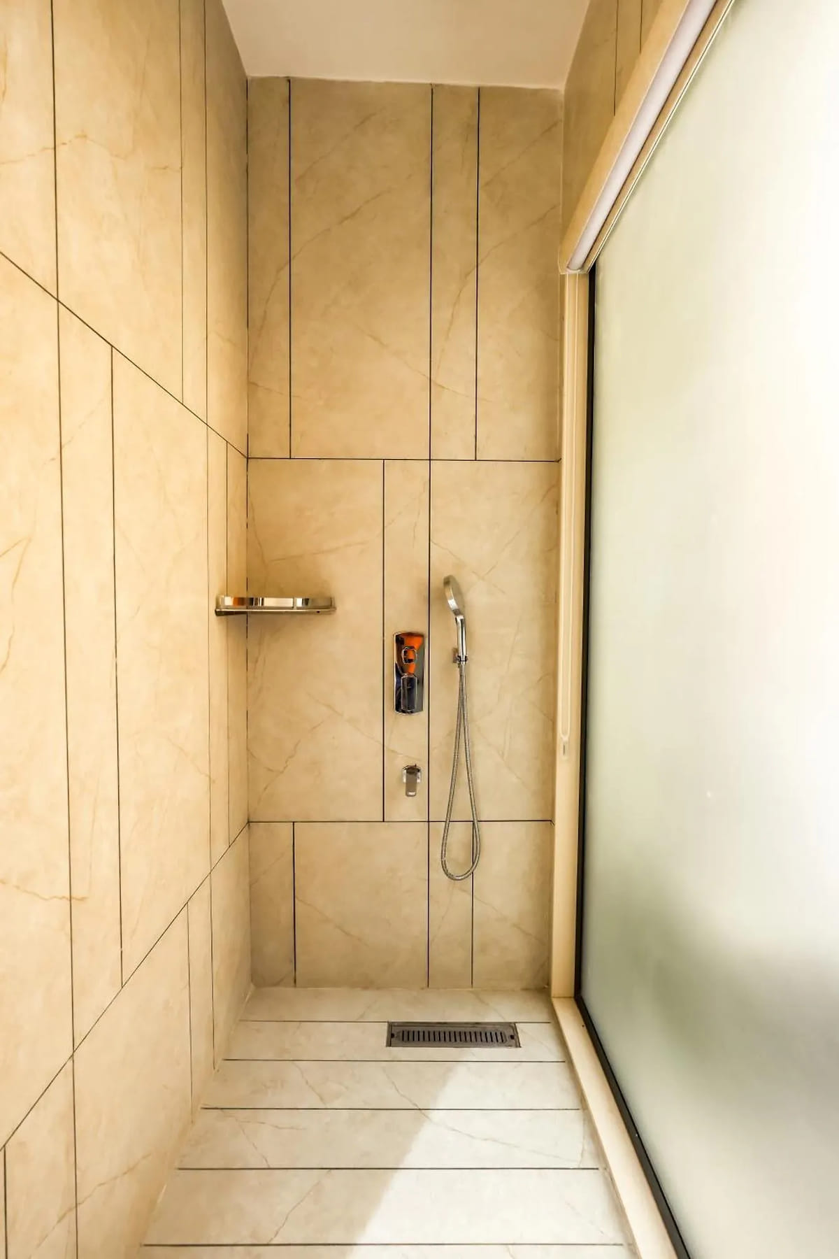 The walk-in shower in a guest bathroom at Marrion Hotel, lined in beige marble-effect tiles with a hand shower