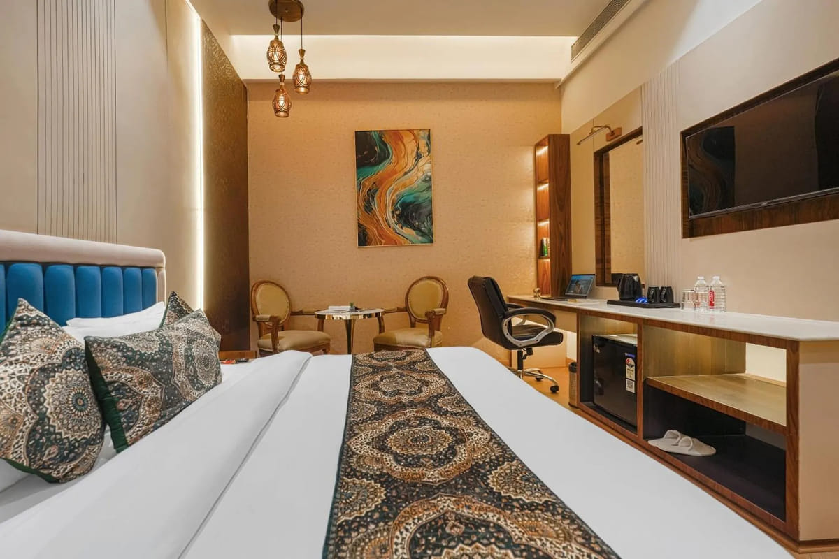 A Deluxe room at Marrion Hotel, with a teal padded headboard, pendant lights, two armchairs by the window and a long desk