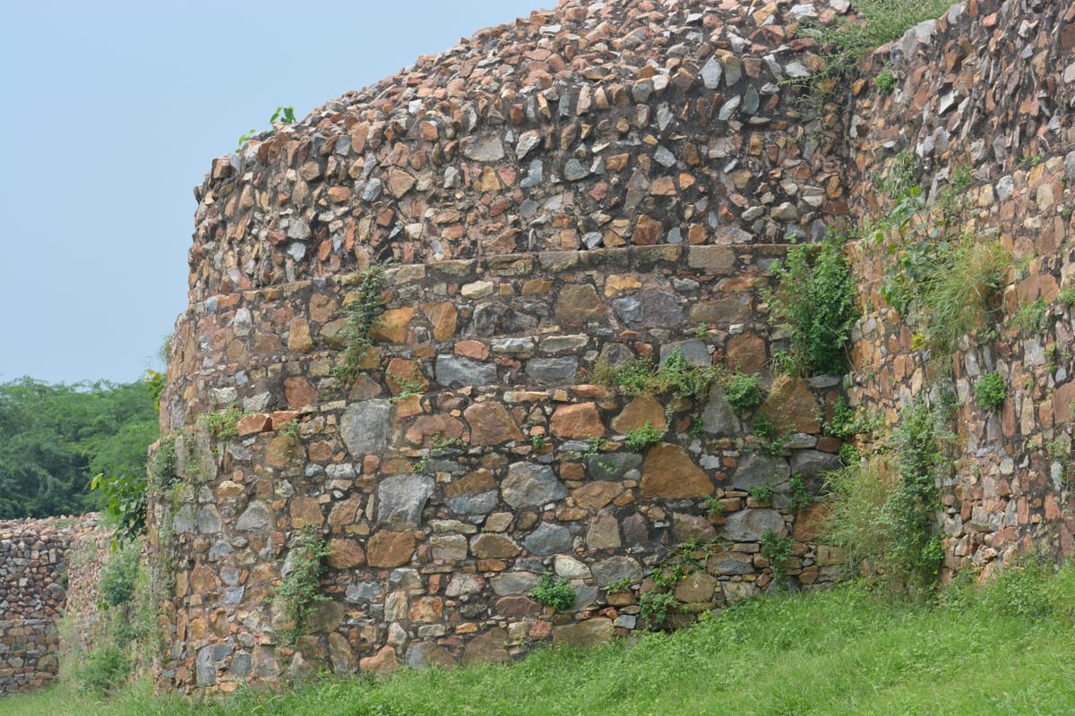 The rubble-stone ramparts of Kangra Fort standing above a grassy slope