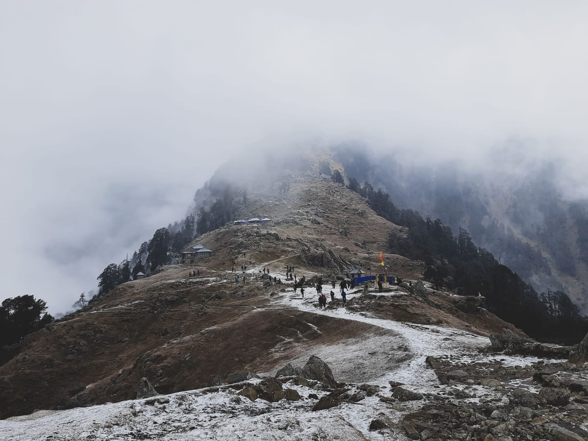 The ridge at Triund above McLeod Ganj, walkers strung along the crest with cloud drifting across the mountainside behind