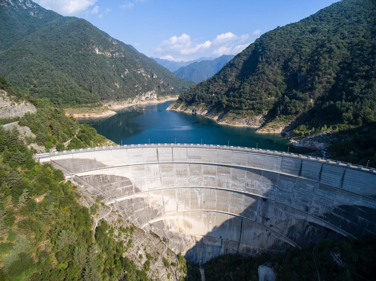 A curved concrete arch dam spanning a forested river gorge