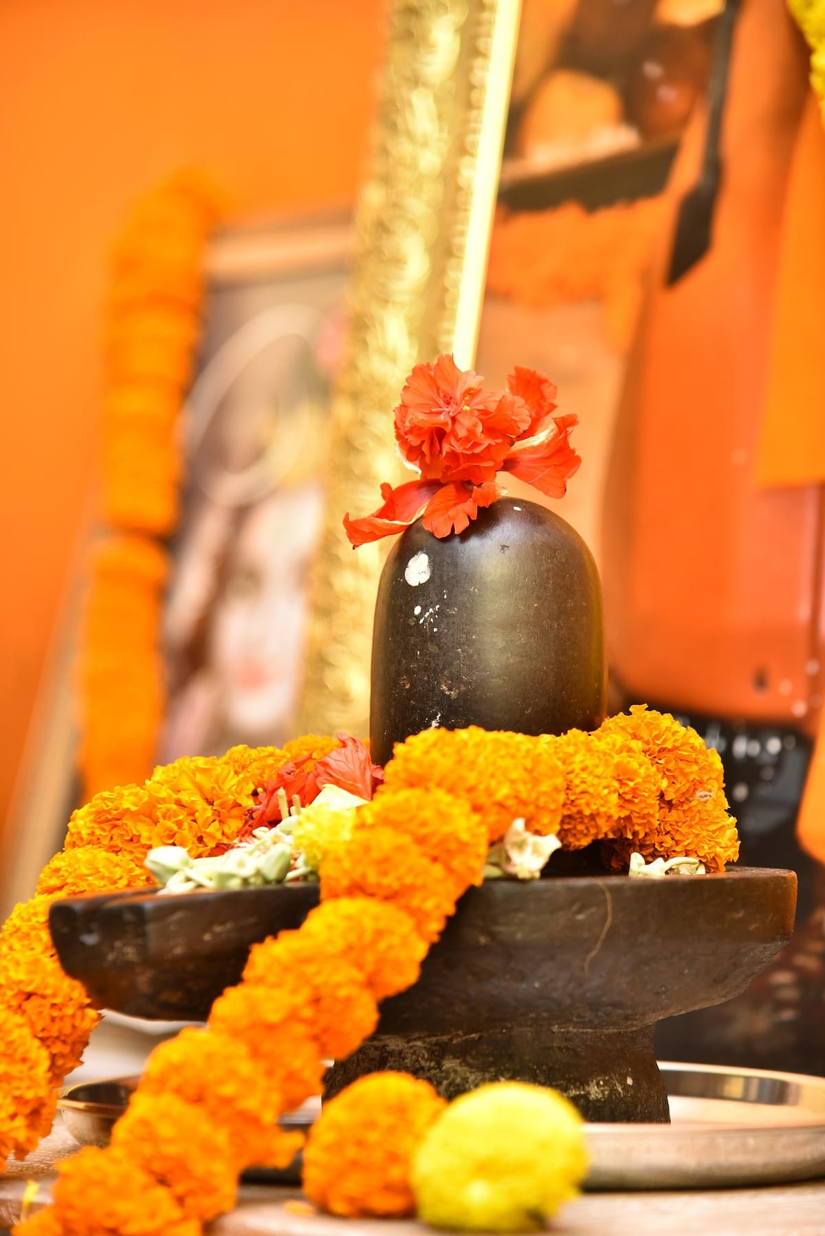 A black stone Shiva lingam draped in marigold garlands with offerings arranged