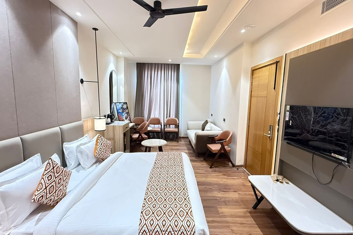 A large guest room at Amara Portico in Amritsar, with a wide bed under a padded headboard, a desk and mirror along one wall