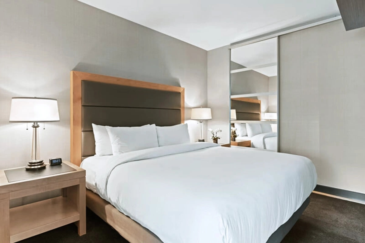A guest room at Amara Portico, with a wide bed against a timber headboard, table lamps on both sides and a mirror alongside