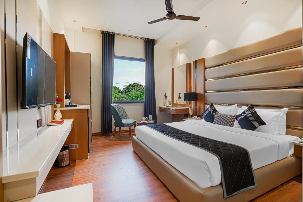 A Deluxe room at Aura Bliss, with a fluted headboard, a dark runner across the bed, a wall-mounted television