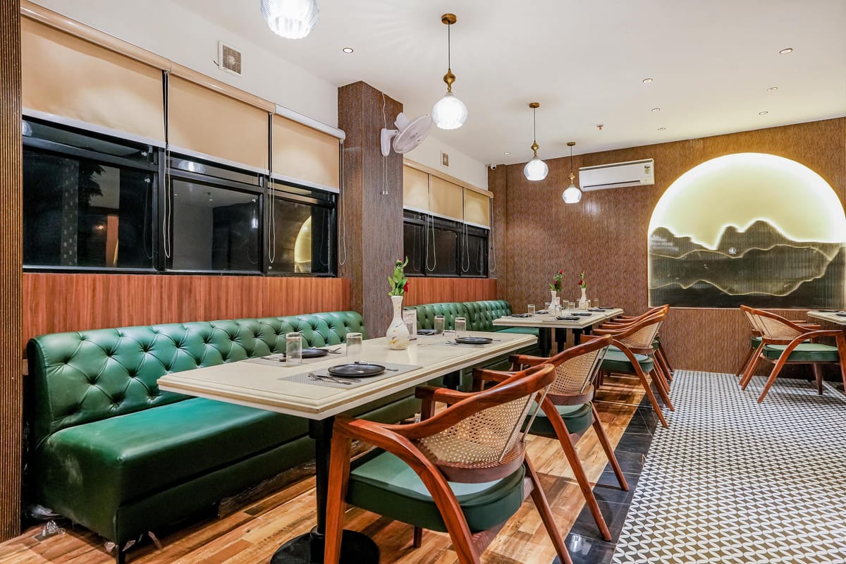 The Restaurant at Aura Bliss, with a green tufted banquette running along tables and wooden chairs, below pendant lights