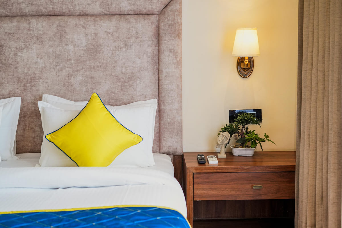 A Deluxe room at Escala Hotel, with a yellow cushion on the bed, a wall lamp above the bedside table and a potted plant