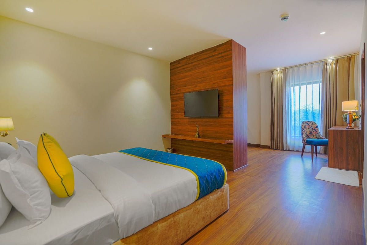 A Suite at Escala Hotel, with a wall-mounted television on a timber panel facing the bed and a curtained window