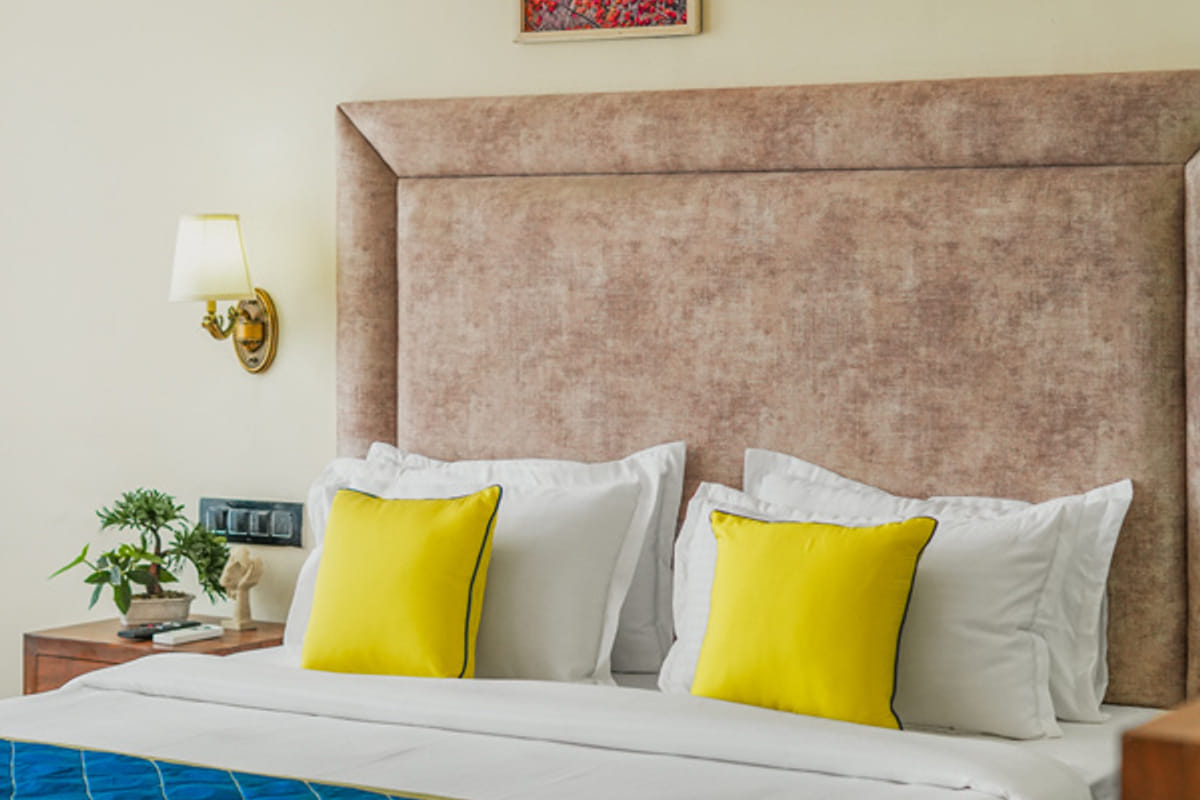 A guest room at Escala Hotel, with a tall padded headboard, yellow cushions on white bedding and two framed prints hung