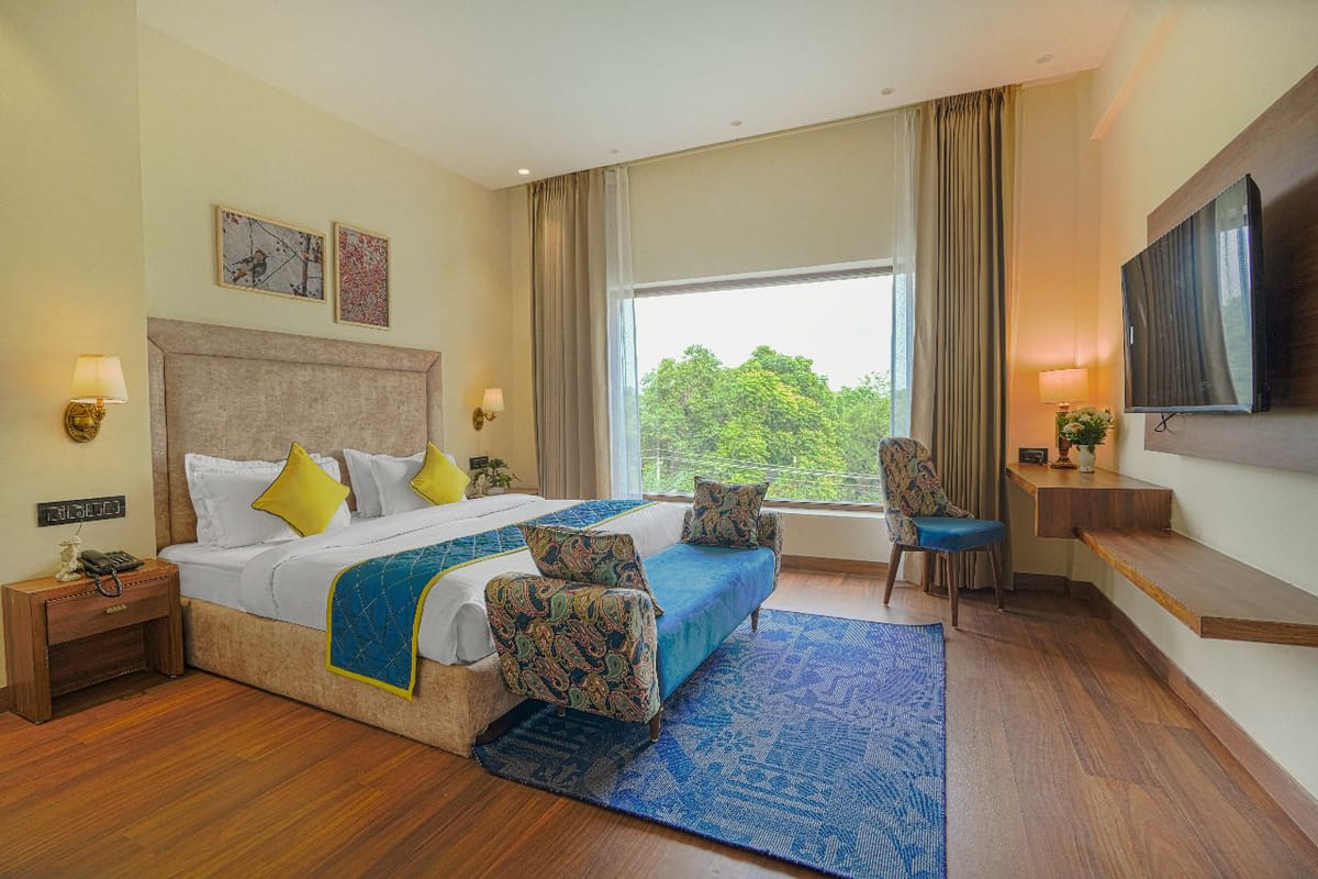 A Super Deluxe room at Escala Hotel, with a blue bed runner, a patterned armchair, a television opposite